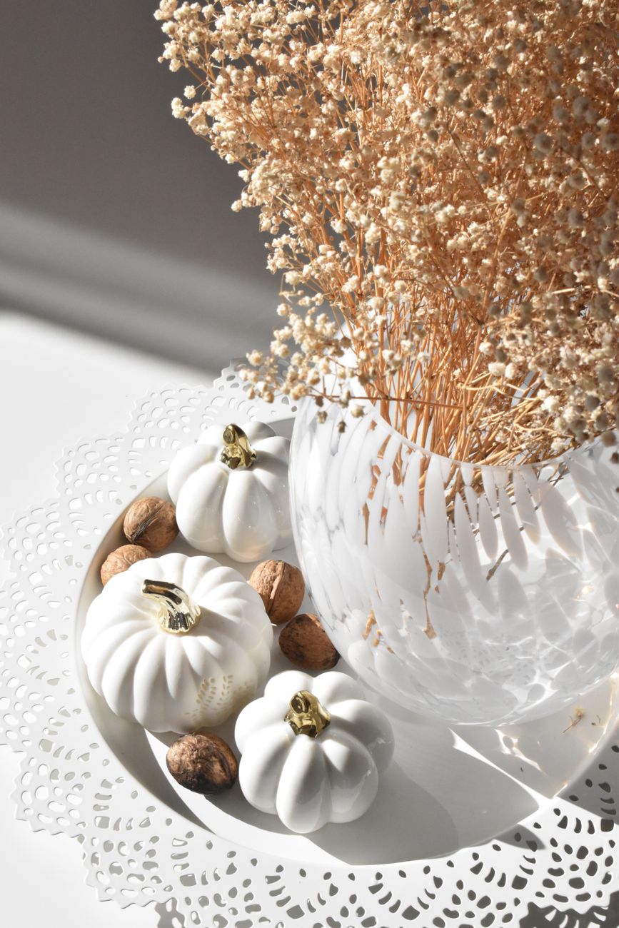 dried flowers in a vase standing next to white pumpkins and walnuts decorations